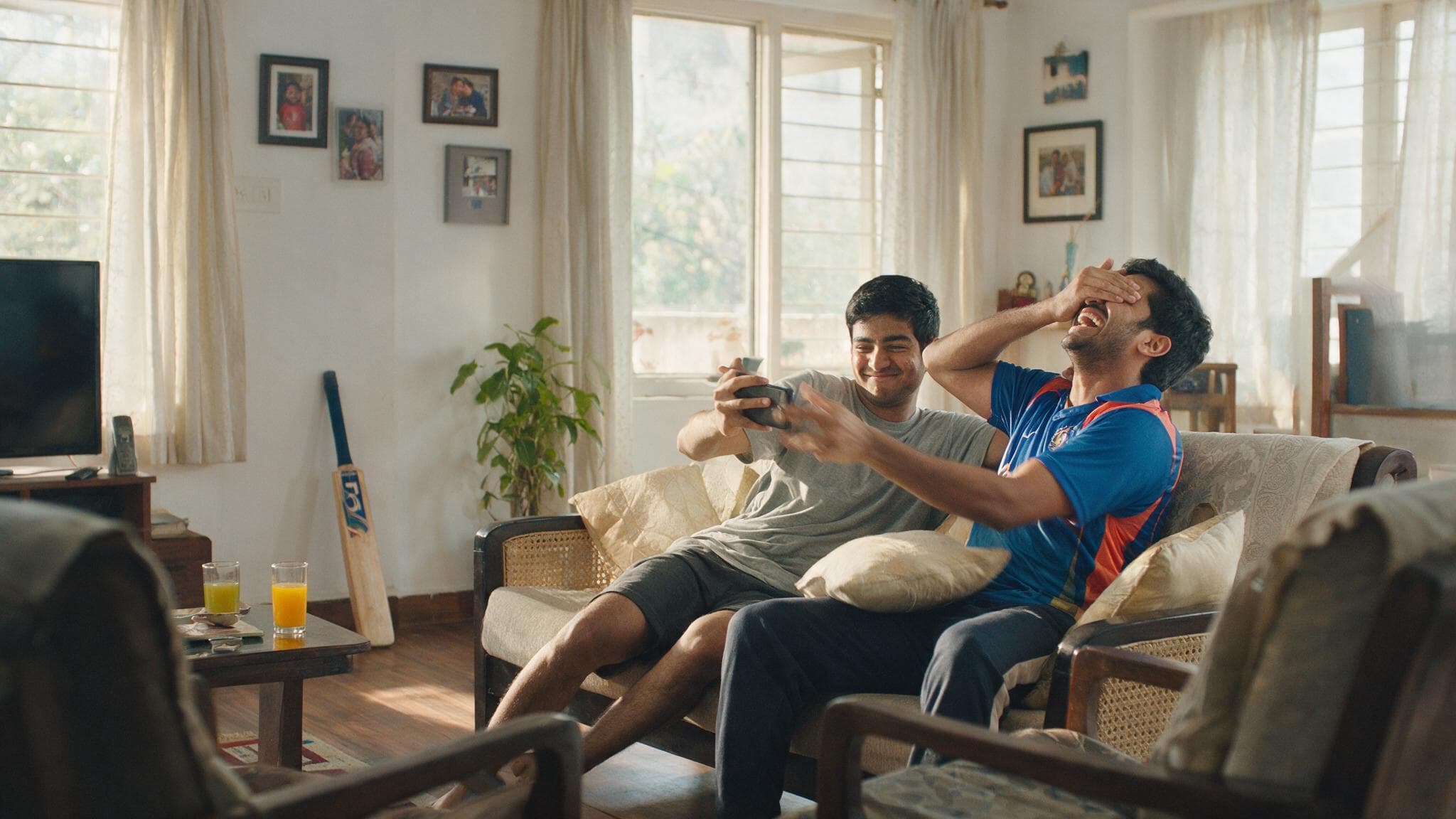 Two brothers laughing on a sofa, one showing his phone while the other reaches to grab it
