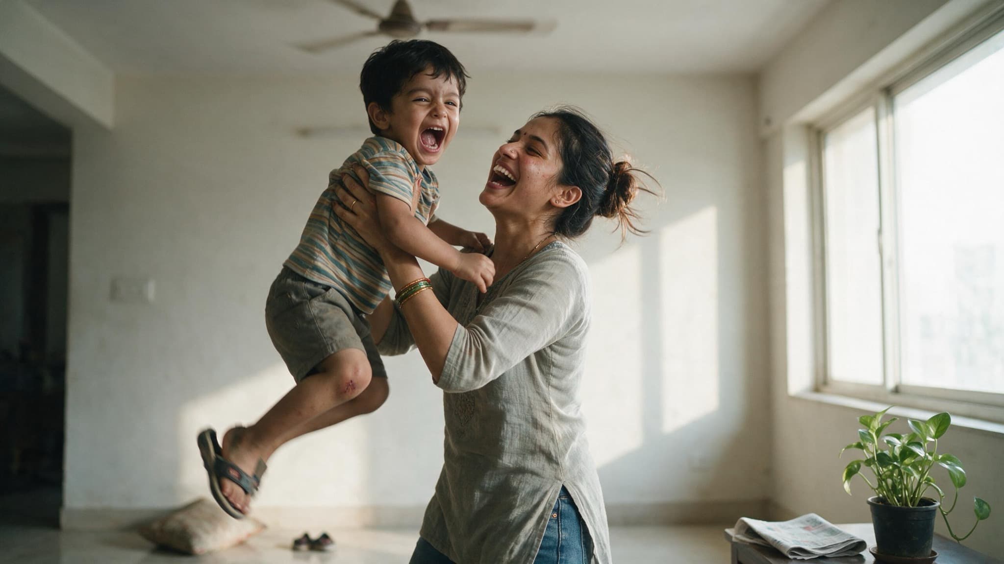 A young Indian woman lifting her small nephew up in a bright living room while both laugh